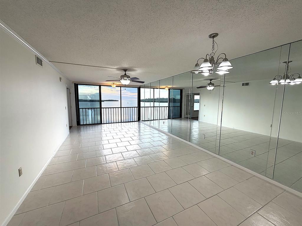 A living room with light tile flooring, mirrored walls, a ceiling fan, and a balcony view — 4620 BAY BOULEVARD UNIT 1122, PORT RICHEY, FL