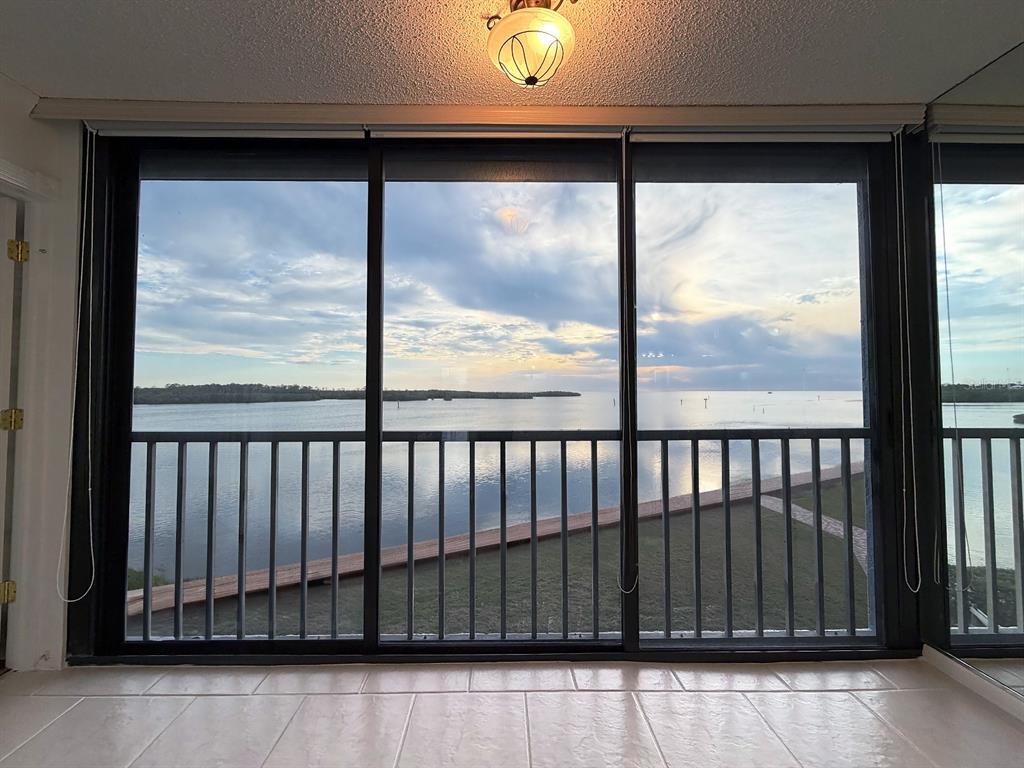 A tiled room features a large sliding glass door overlooking a waterfront view and balcony — 4620 BAY BOULEVARD UNIT 1122, PORT RICHEY, FL