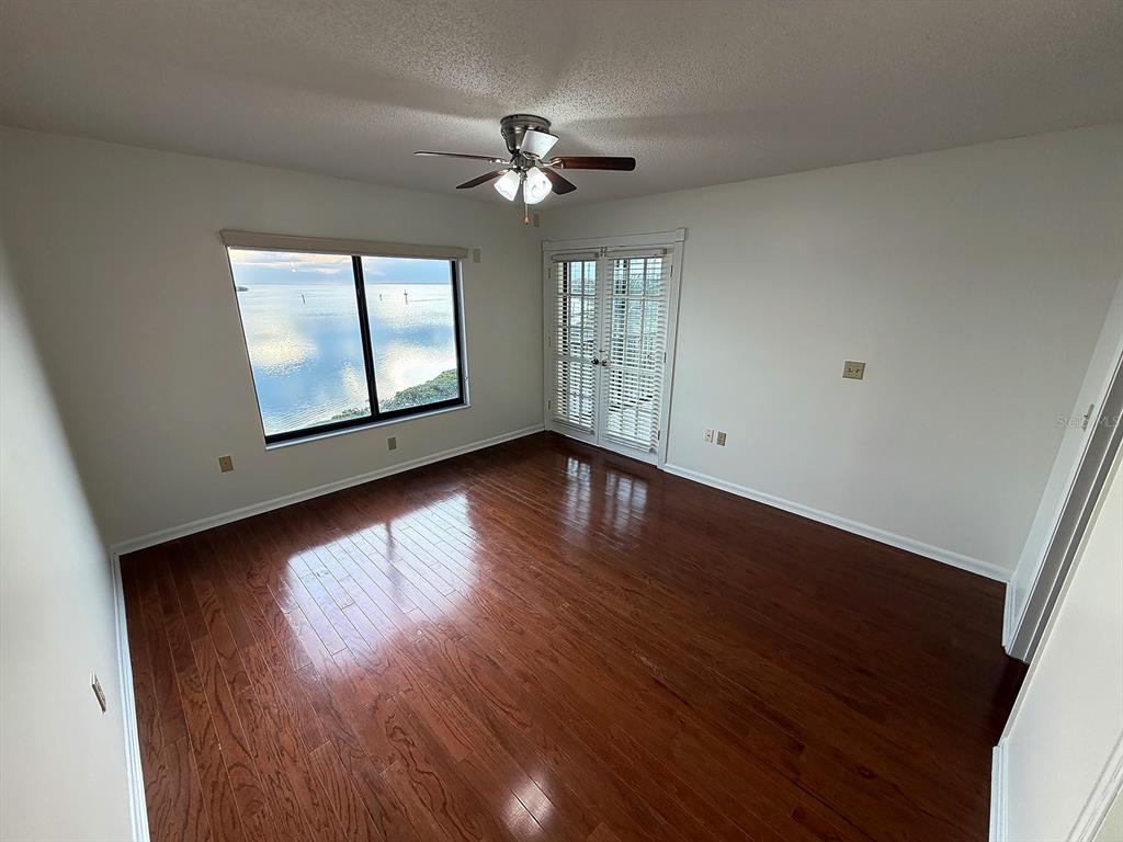 An empty bedroom features hardwood floors, a ceiling fan, a large window, and glass doors — 4620 BAY BOULEVARD UNIT 1122, PORT RICHEY, FL