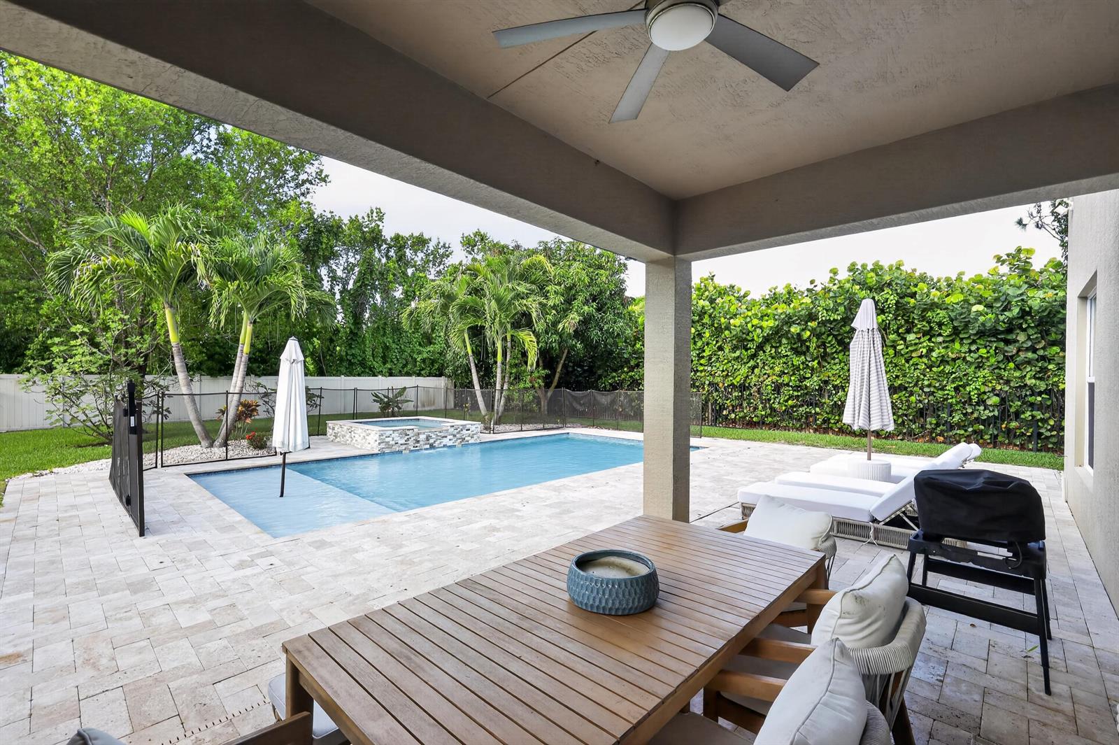 A covered patio overlooks a swimming pool with a spa and lounge chairs in a backyard — 7050 Limestone Cay Road, FL 33458, FL