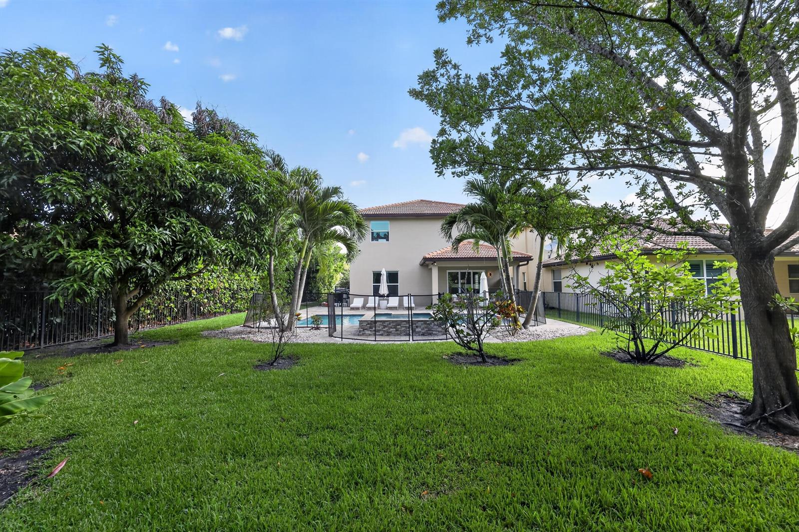 A backyard features a swimming pool with a safety fence, palm trees, and green lawn — 7050 Limestone Cay Road, FL 33458, FL