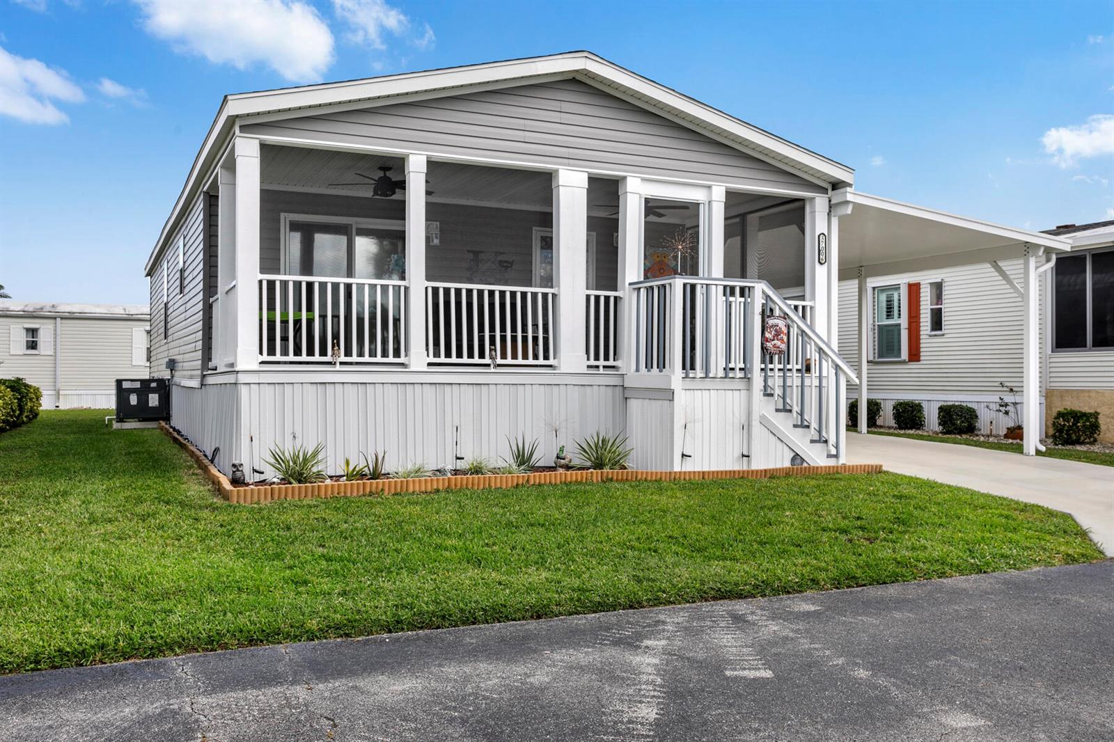 A light gray manufactured home features a screened-in front porch and an attached carport — 37006 Exuma Bay, Boynton Beach FL 33436, BOYNTON BEACH, FL