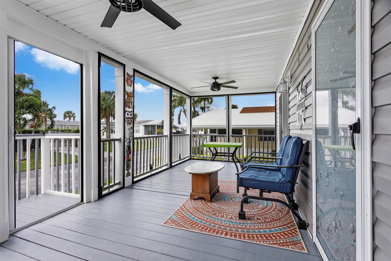 A screened-in porch features gray wood flooring, two blue chairs, a rug, and ceiling fans — 37006 Exuma Bay, Boynton Beach FL 33436, BOYNTON BEACH, FL