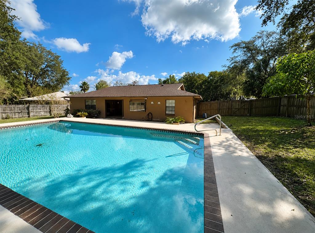 A backyard featuring a swimming pool, a tan house, and a wooden privacy fence — 226 COUNCIL BLUFFS DRIVE, DELTONA, FL