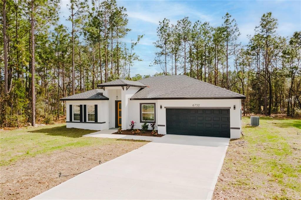 A single-story white house with a dark garage door and a concrete driveway — 6732 SW 132ND STREET, OCALA, FL
