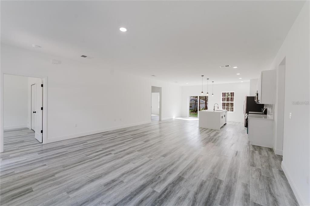 An open-concept living area features light gray wood-look flooring, white walls, and a kitchen island — 6732 SW 132ND STREET, OCALA, FL