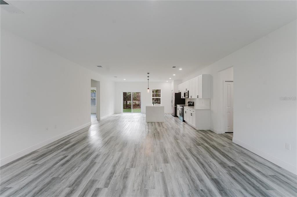 An open-concept kitchen and living area features white cabinetry, a center island, and wood-look flooring — 6732 SW 132ND STREET, OCALA, FL