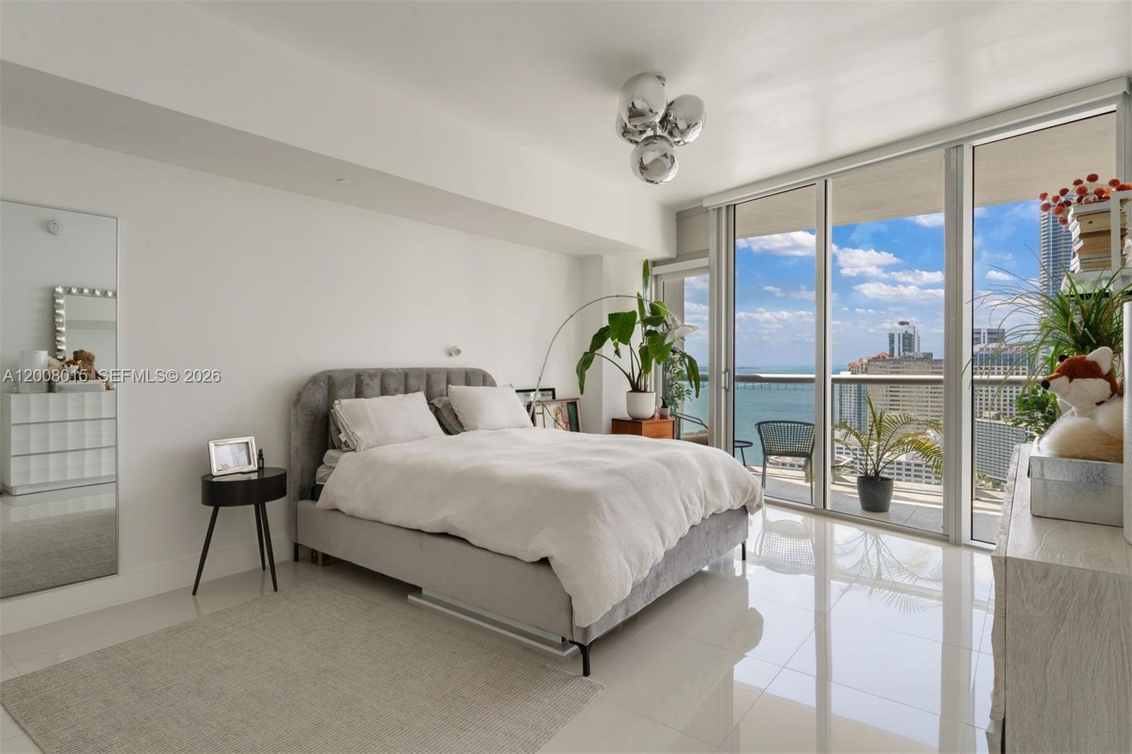 A modern bedroom with a grey upholstered bed, white tile floors, and floor-to-ceiling balcony windows — 495 Brickell Ave # 3509, Miami FL 33131, MIAMI, FL