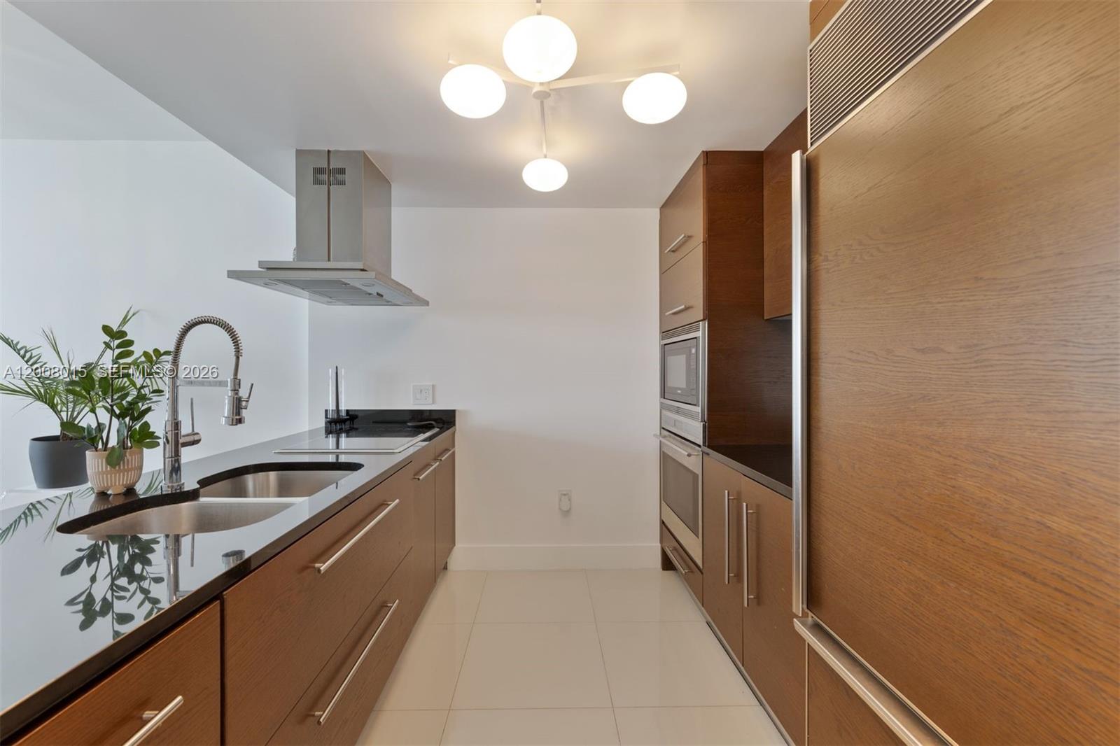 A galley kitchen features wood-grain cabinetry, black countertops, stainless steel appliances, and white tile flooring — 495 Brickell Ave # 3509, Miami FL 33131, MIAMI, FL