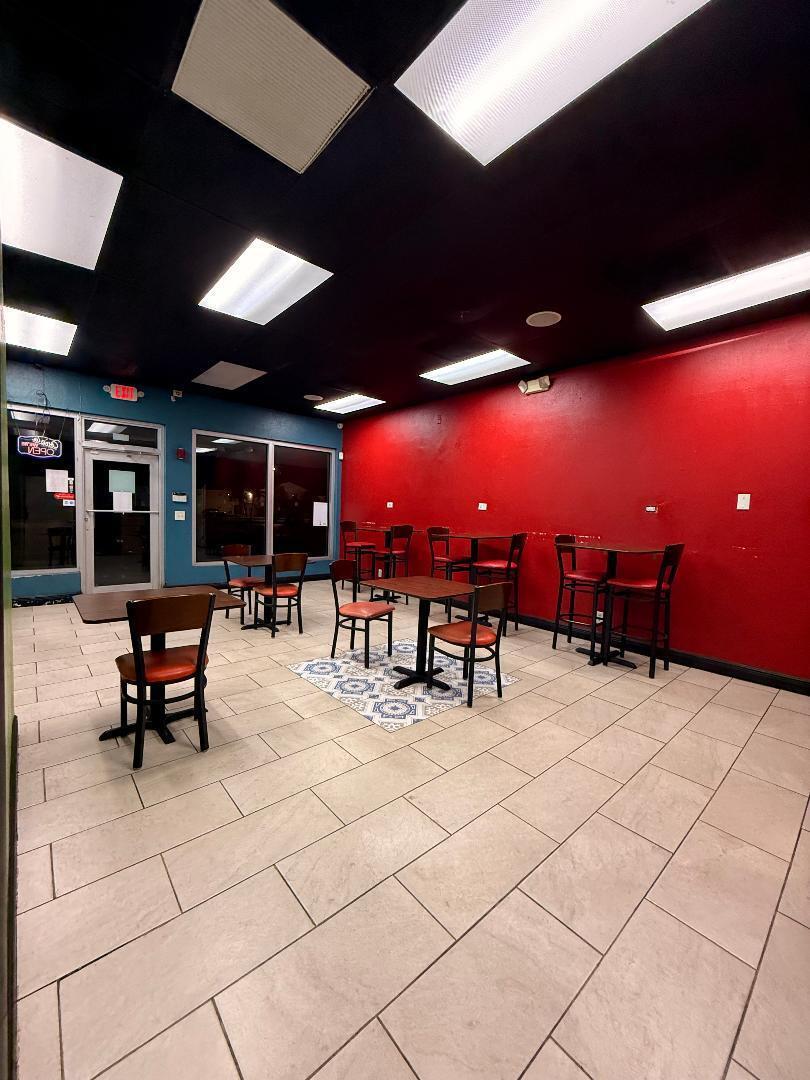 A commercial dining area features red and blue walls, tile flooring, and several small tables — 9999 W Blue Heron Boulevard, Riviera Beach FL 33404, RIVIERA BEACH, FL