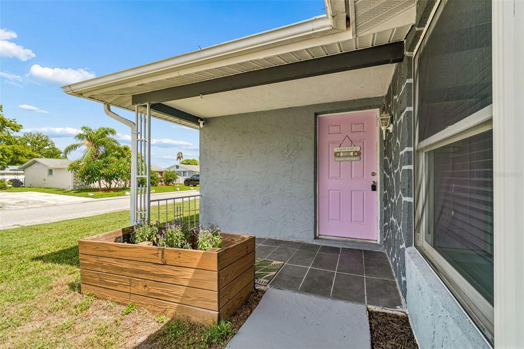 A covered porch features a pink front door, dark tiled flooring, and a wooden planter box — 9140 COCHISE LANE, PORT RICHEY, FL