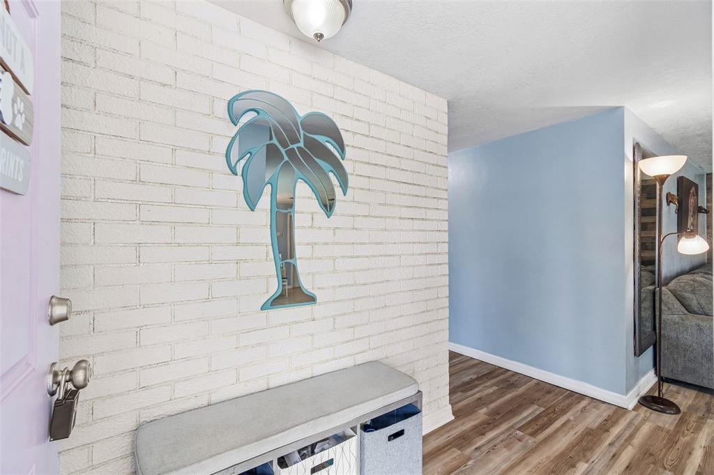 A white brick wall features a palm tree mirror above a storage bench in an entryway — 9140 COCHISE LANE, PORT RICHEY, FL