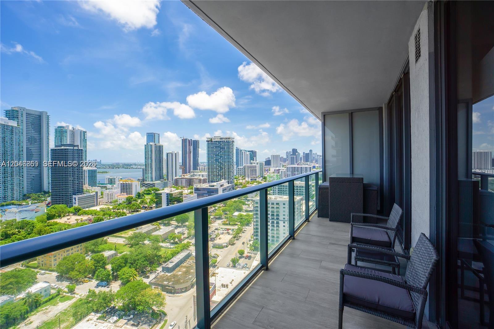 A high-rise balcony features outdoor seating and a panoramic view of a city skyline — 121 NE 34th St # 2706, Miami FL 33137, MIAMI, FL