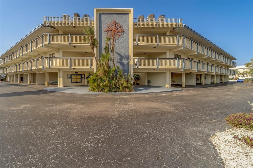 A three-story apartment building with covered parking and a compass rose mural on the exterior — 11650 CAPRI CIRCLE S UNIT 105, TREASURE ISLAND, FL