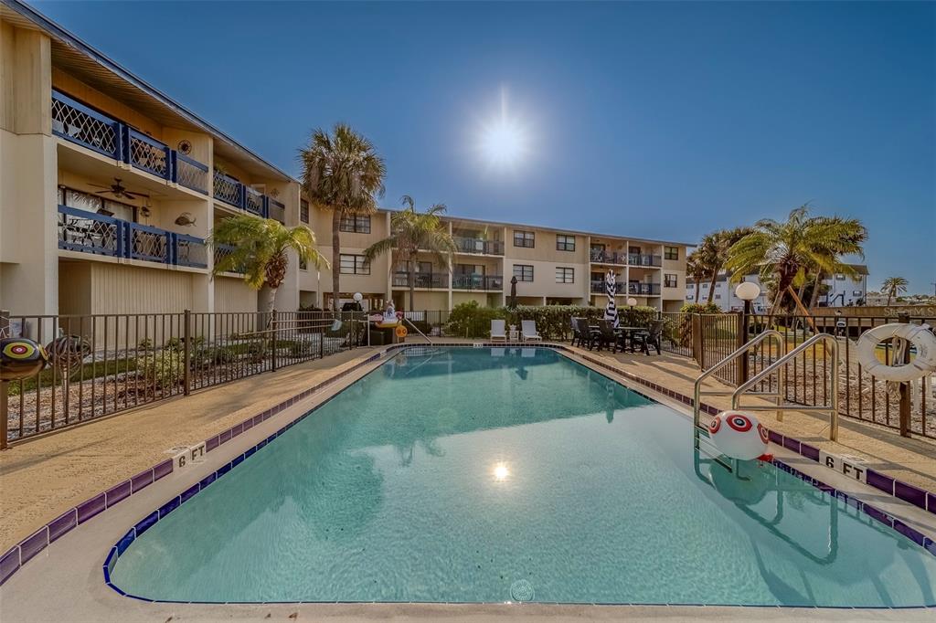 A rectangular swimming pool sits in front of a multi-story apartment building with balconies — 11650 CAPRI CIRCLE S UNIT 105, TREASURE ISLAND, FL