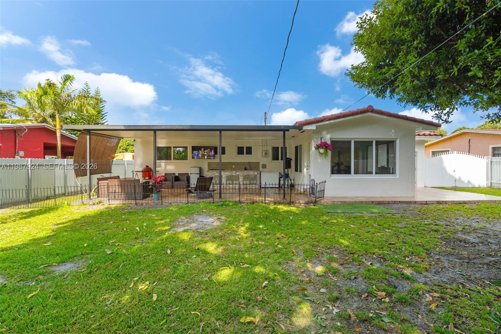 A backyard view of a house with a covered patio, outdoor kitchen, and fenced lawn — 10747 NW 22nd Ct, Miami FL 33167, MIAMI, FL