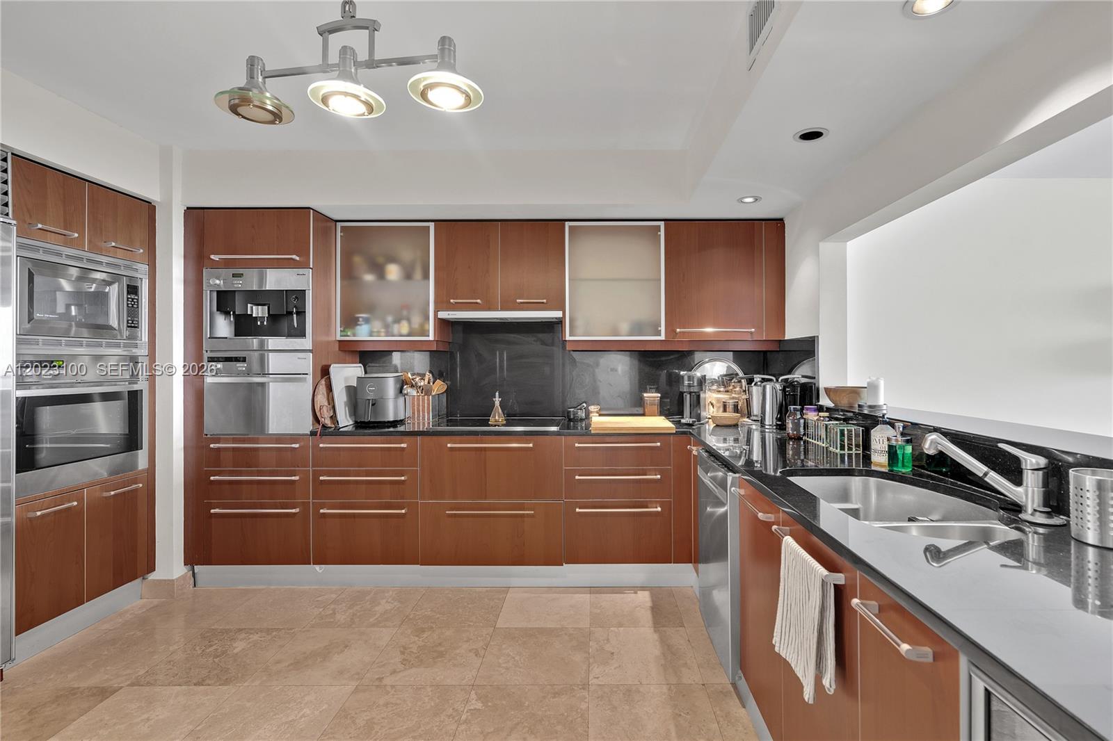A modern kitchen features wood cabinets, black countertops, stainless steel appliances, and tile flooring — 1331 Brickell Bay Dr # 2007, Miami FL 33131, MIAMI, FL