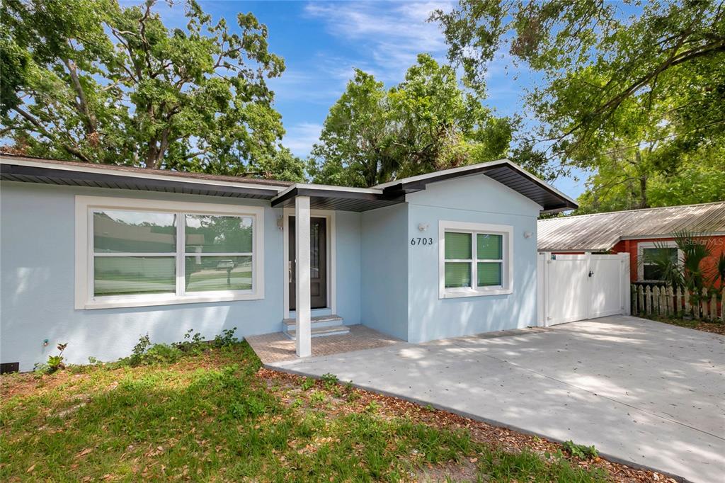 A light blue single-story house features a concrete driveway, white trim, and a covered entryway — 6703 N BOULEVARD, TAMPA, FL