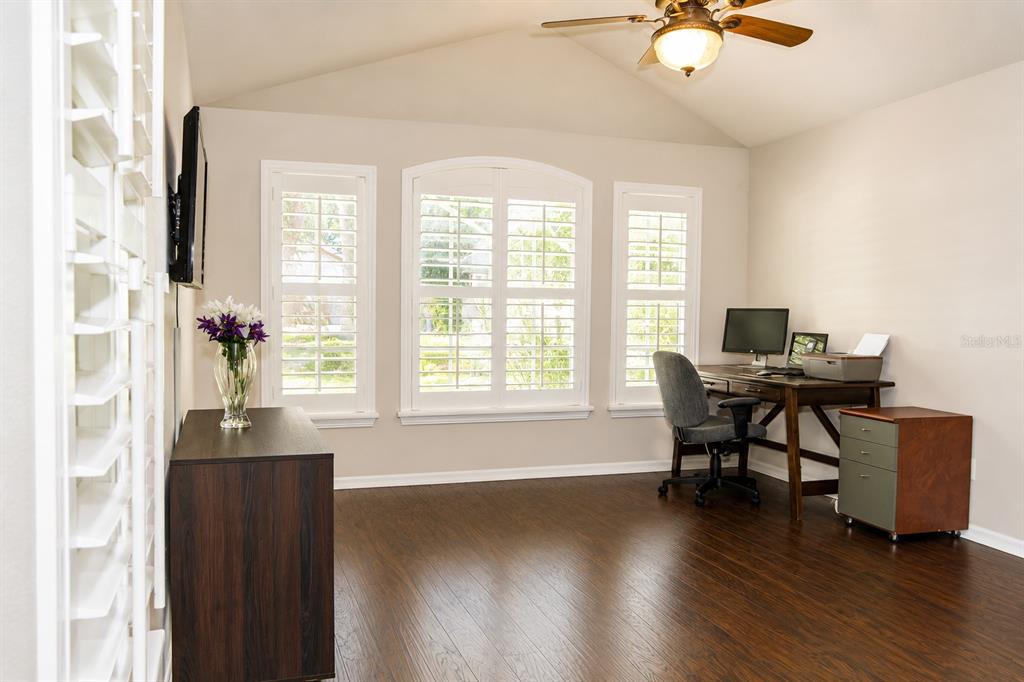A home office with dark wood floors, three windows with shutters, and a wooden desk — 10839 NEWBRIDGE DRIVE, RIVERVIEW, FL