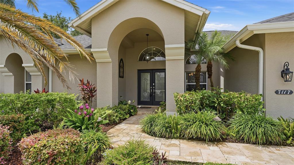 A single-story house with a beige stucco exterior, a two-car garage, and a palm tree — 7117 DORNOUGH LANE, BRADENTON, FL