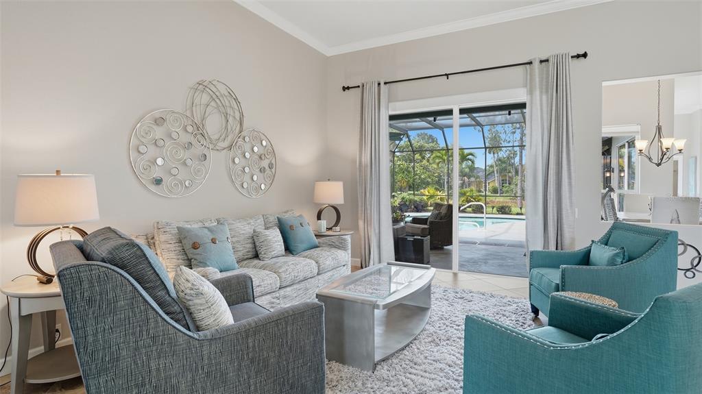 A living room features a sofa, two teal armchairs, and a sliding door to a pool — 7117 DORNOUGH LANE, BRADENTON, FL