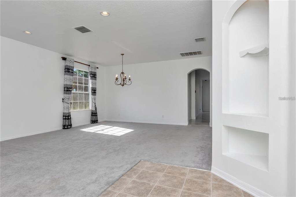 A carpeted dining room features a chandelier, a window with curtains, and a built-in niche — 29822 BOYETTE OAKS PLACE, WESLEY CHAPEL, FL