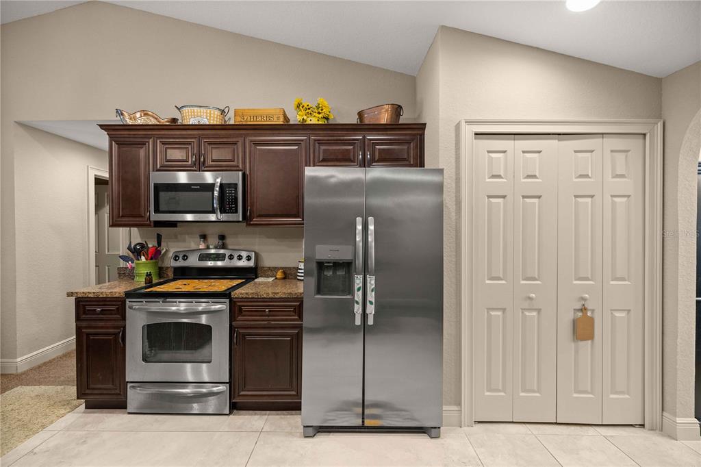 A kitchen features dark wood cabinets, stainless steel appliances, and a beige pantry door — 162 GUAVA TERRACE, OCKLAWAHA, FL
