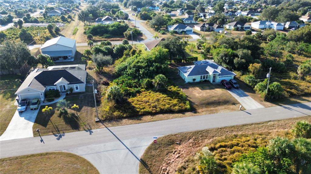 An aerial view shows two suburban houses separated by a large, overgrown vacant lot — LOT 25, LEOPOLD AVENUE, NORTH PORT, FL