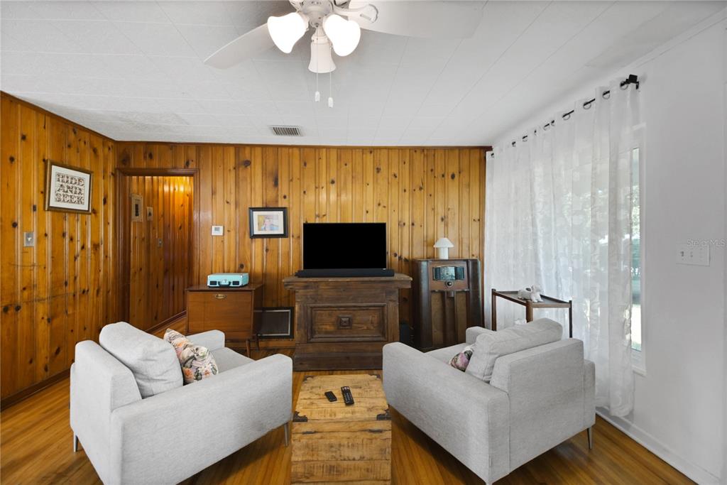 A living room features wood-paneled walls, two gray armchairs, a wooden coffee table, and a television — 114 PARK AVENUE, FRUITLAND PARK, FL