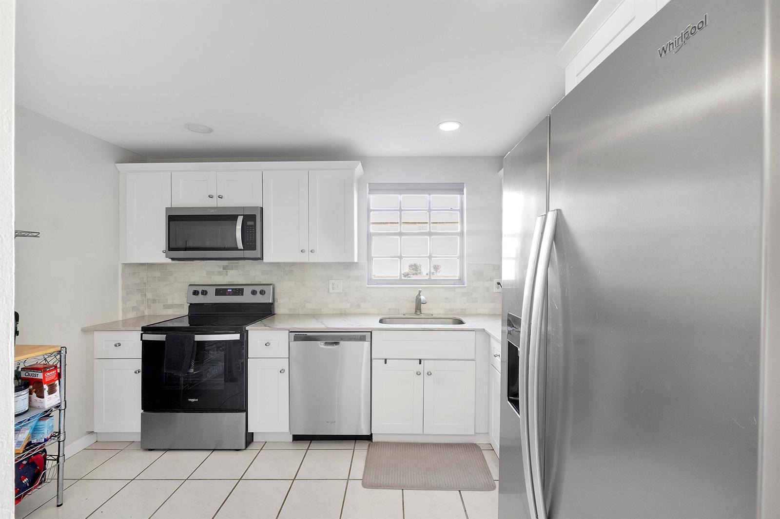 A kitchen with white cabinets, stainless steel appliances, a tiled backsplash, and light floor tiles — 1700 Dover Road # a, Delray Beach FL 33445, DELRAY BEACH, FL