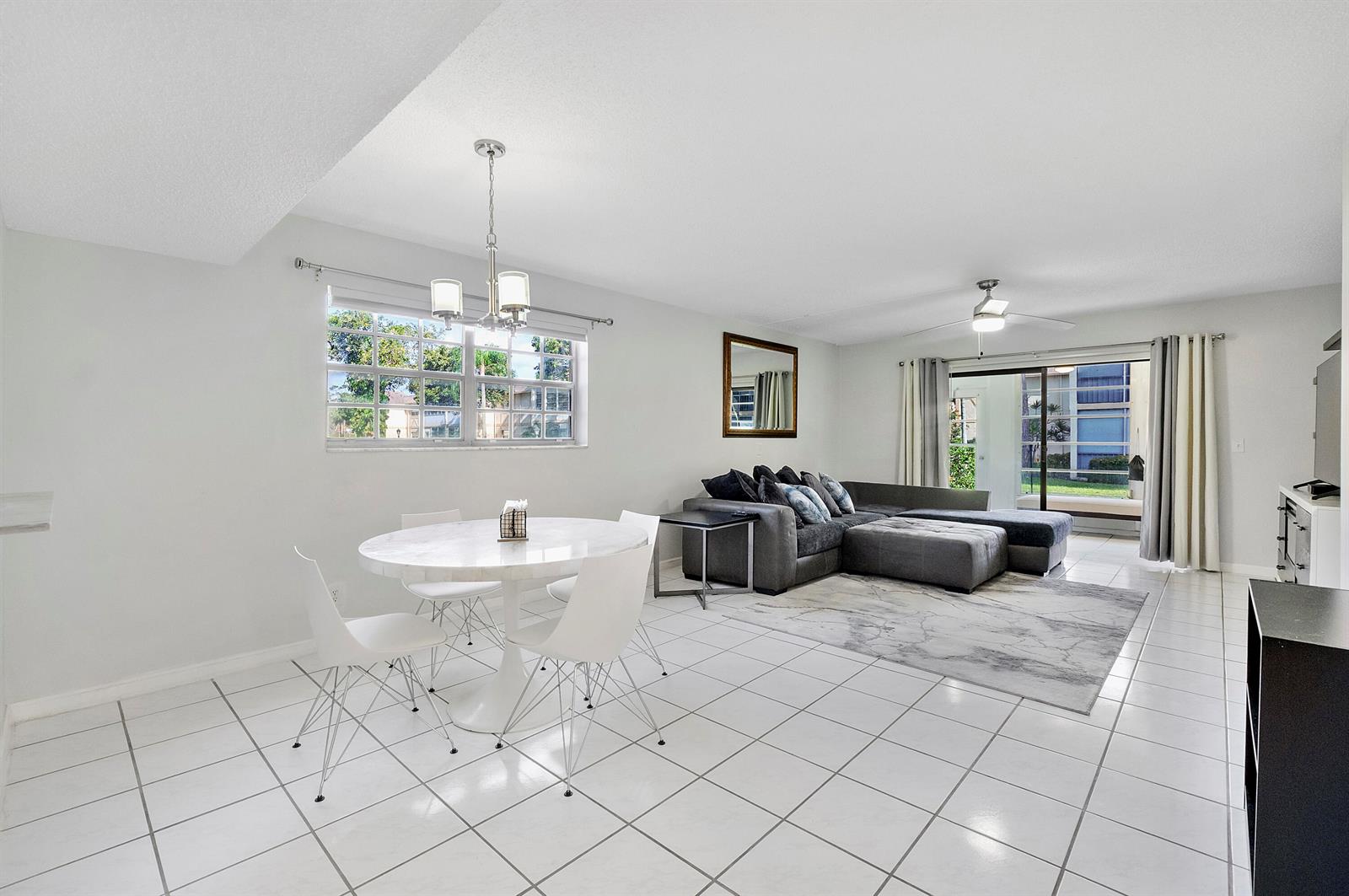 An open-concept living and dining area features white tile floors, a round table, and sectional — 1700 Dover Road # a, Delray Beach FL 33445, DELRAY BEACH, FL