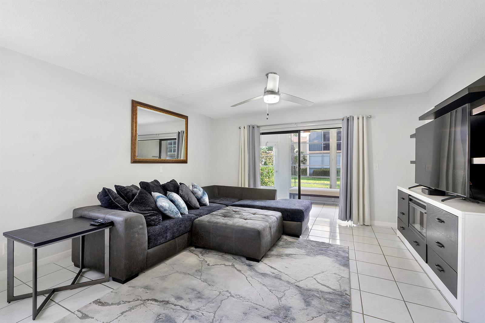 A living room features a gray sectional sofa, a television console, and sliding glass doors — 1700 Dover Road # a, Delray Beach FL 33445, DELRAY BEACH, FL