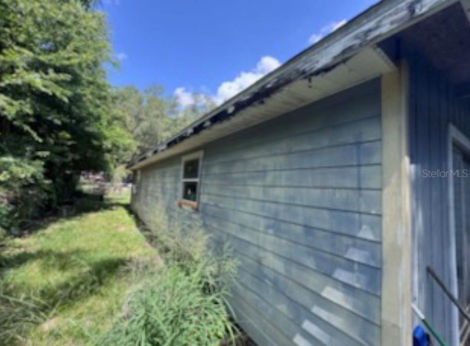 The side exterior of a blue house shows weathered siding and damaged roof eaves — 38124 ILLINOIS STREET, LADY LAKE, FL