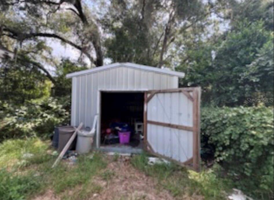 A metal storage shed with an open door stands in a yard surrounded by trees — 38124 ILLINOIS STREET, LADY LAKE, FL