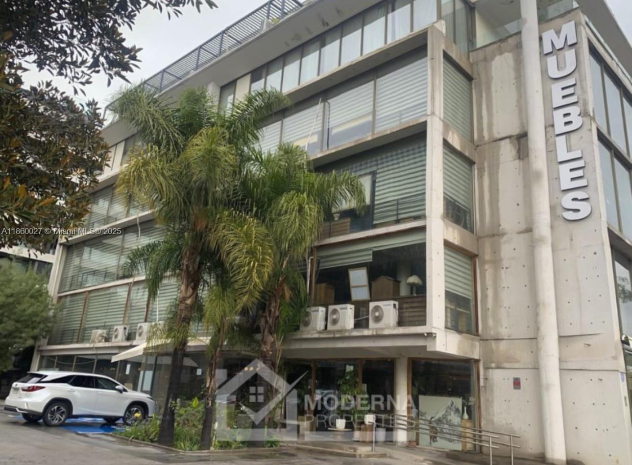 A multi-story commercial building with a concrete facade and large windows features a palm tree — Avda. Las Condes 10.527, 8320269, FL