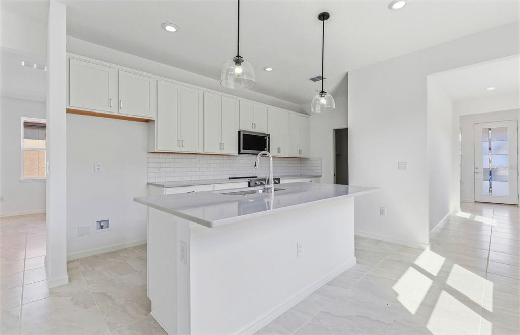 A modern kitchen features white cabinets, a central island with a sink, and tile flooring — 5958 SW 86TH AVENUE ROAD, OCALA, FL