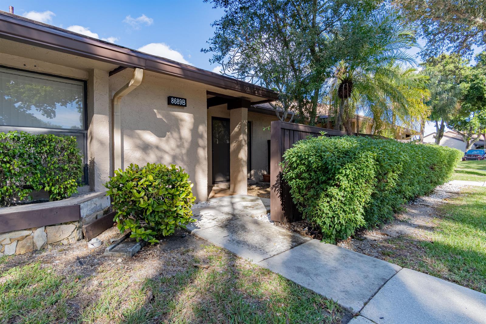 A tan exterior of a single-story home features a walkway, landscaping, and a dark fence — 8689 W Boca Glades Boulevard W # B, Boca Raton FL 33434, BOCA RATON, FL
