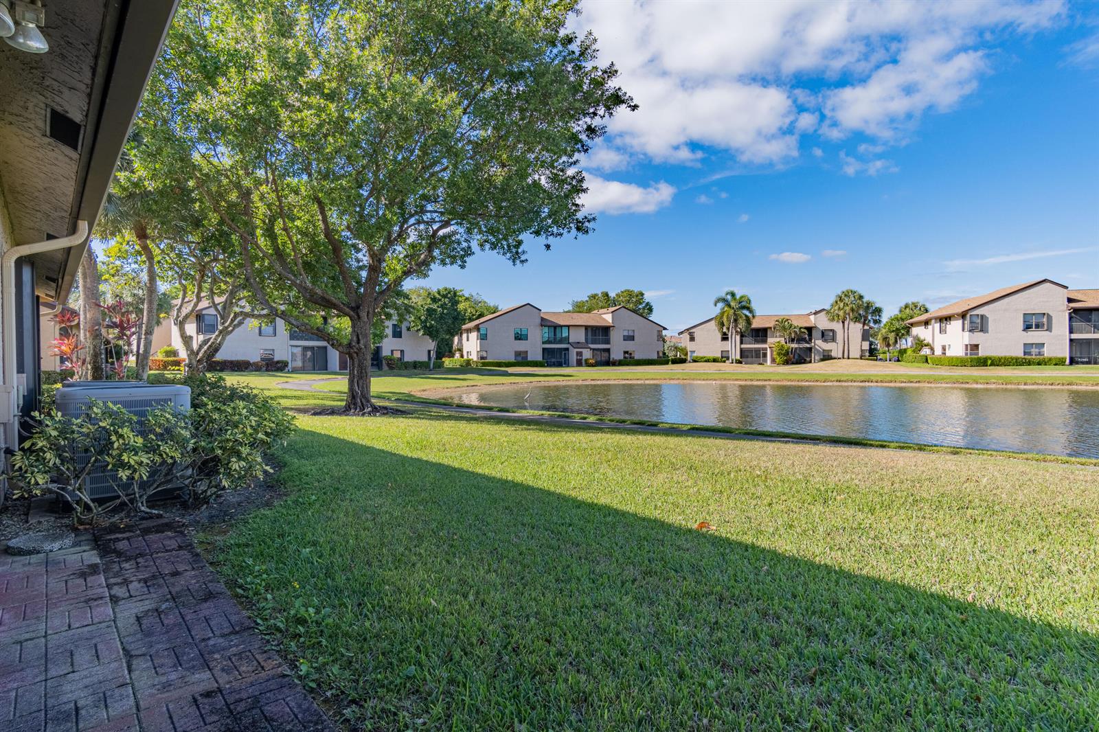 A view of a grassy lawn, a pond, and apartment buildings under a blue sky — 8689 W Boca Glades Boulevard W # B, Boca Raton FL 33434, BOCA RATON, FL