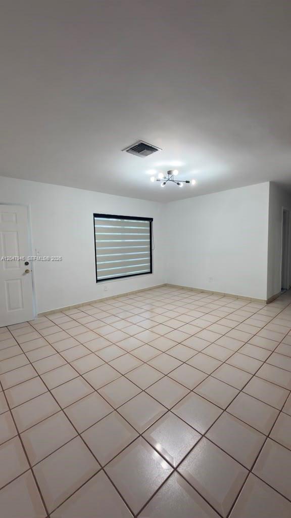 A bright, empty room features white walls, tiled flooring, a window with blinds, and a chandelier — 19200 NW 44th Ave, Miami Gardens FL 33055, MIAMI GARDENS, FL