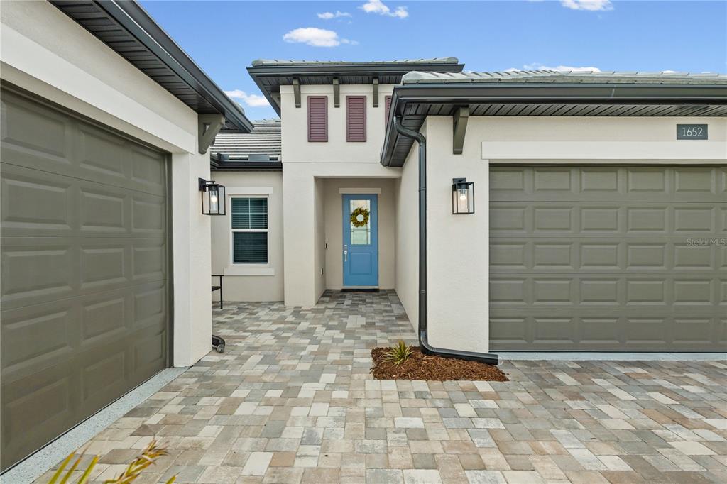 A modern house exterior features a blue front door, paver driveway, and two garage doors — 1652 LUGANO CIRCLE, NOKOMIS, FL