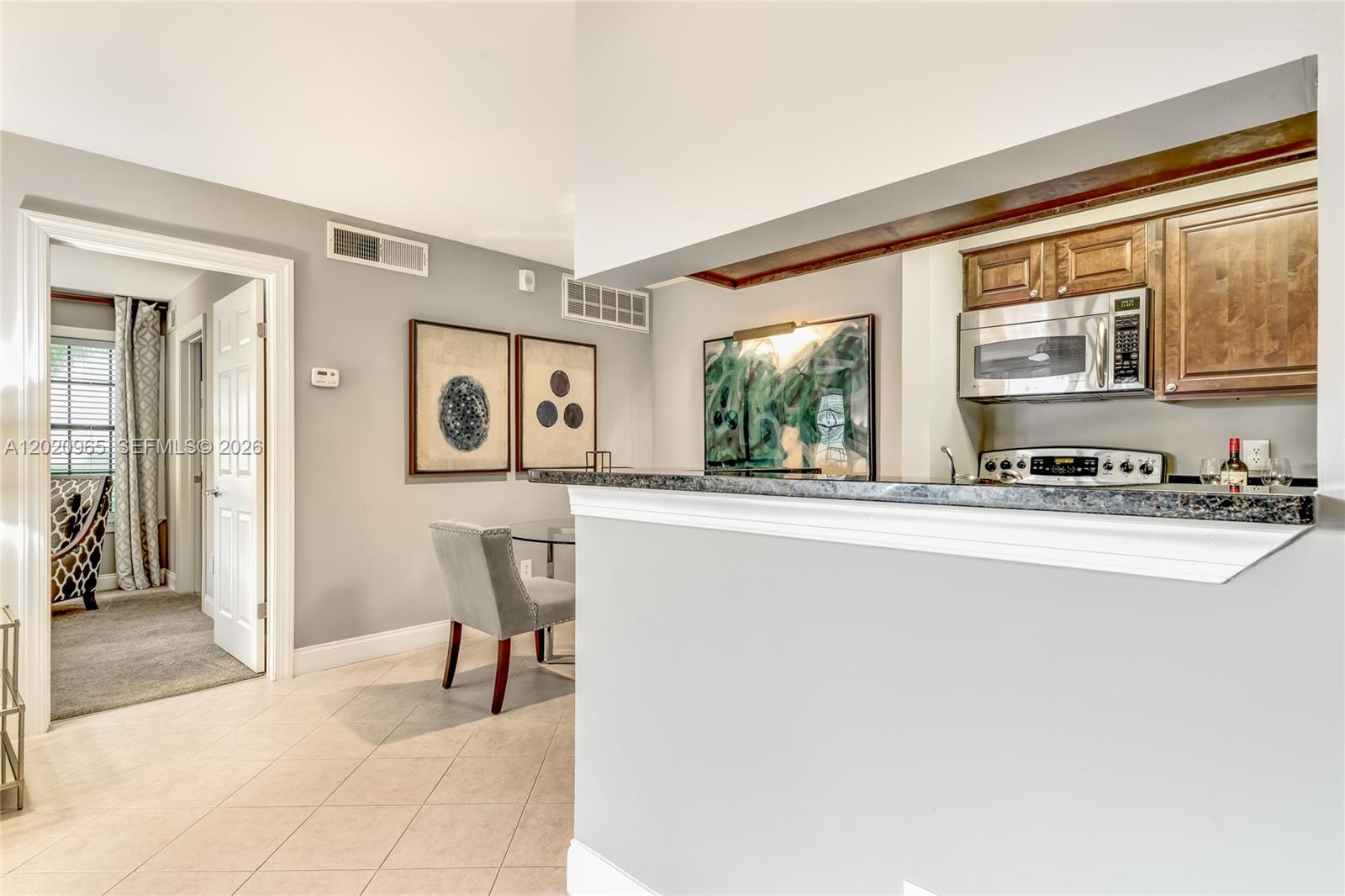 A kitchen with a breakfast bar overlooks a dining area with two framed art pieces — 6503 N Military Trl, Boca Raton FL 33496, BOCA RATON, FL