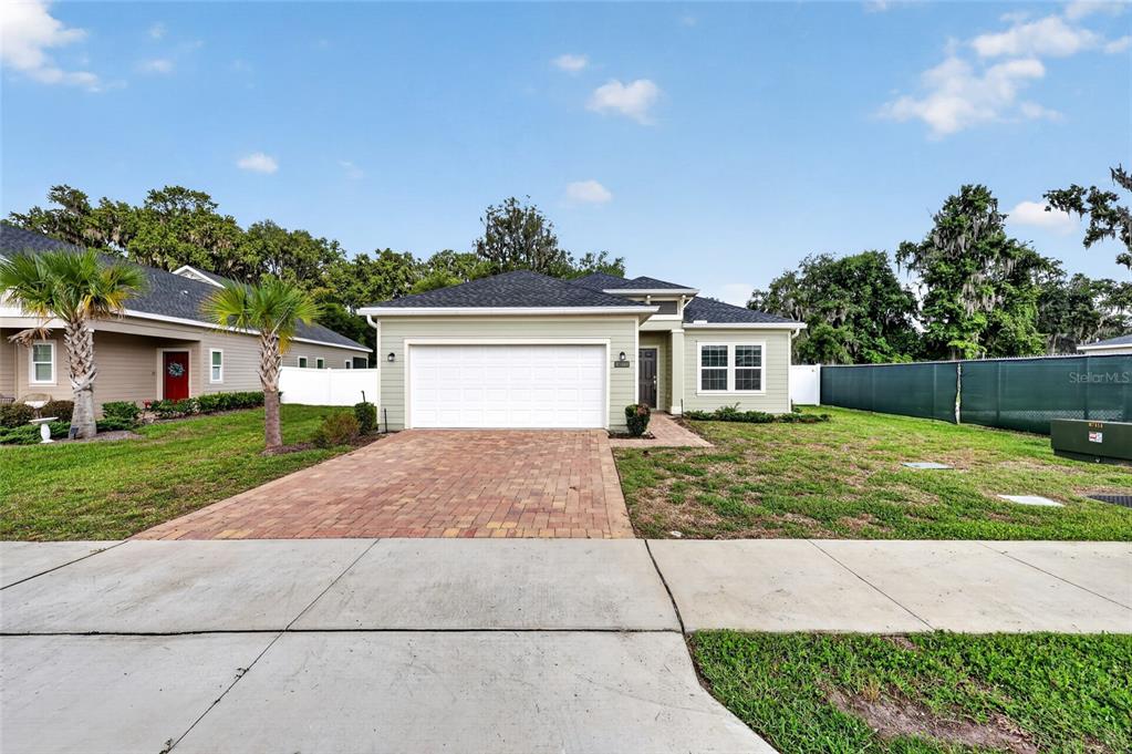 A light green single-story house with a white garage door and a brick paver driveway — 1700 NW 44TH COURT ROAD, OCALA, FL