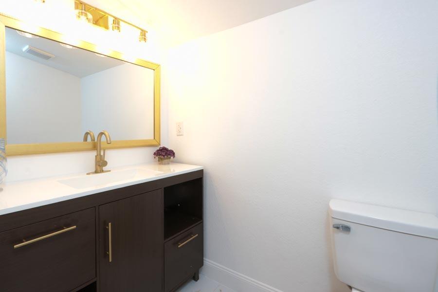 A bathroom features a dark wood vanity with a white countertop, gold faucet, and mirror — 251 Avenue O, Riviera Beach FL 33404, RIVIERA BEACH, FL