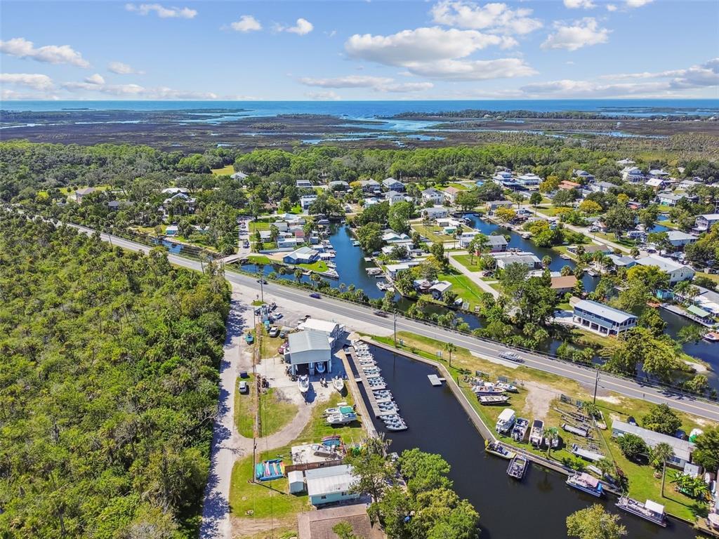 An aerial view shows a coastal neighborhood with houses, a marina, and a road — 7154 SHOAL LINE BOULEVARD, WEEKI WACHEE, FL