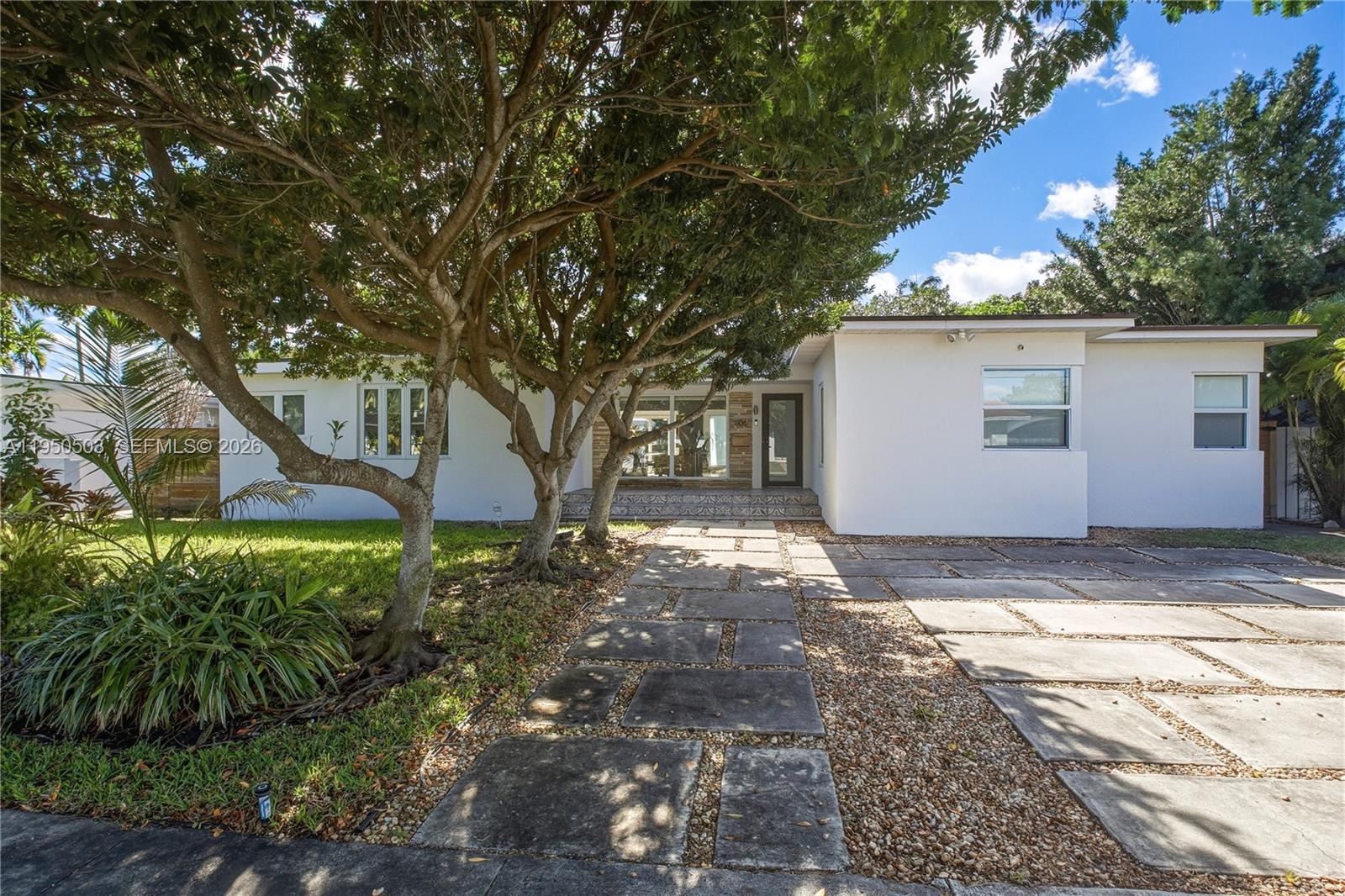 A white single-story house features a stone-paved walkway, a gravel driveway, and mature trees — 1106 NE 86th St, Miami FL 33138, MIAMI, FL