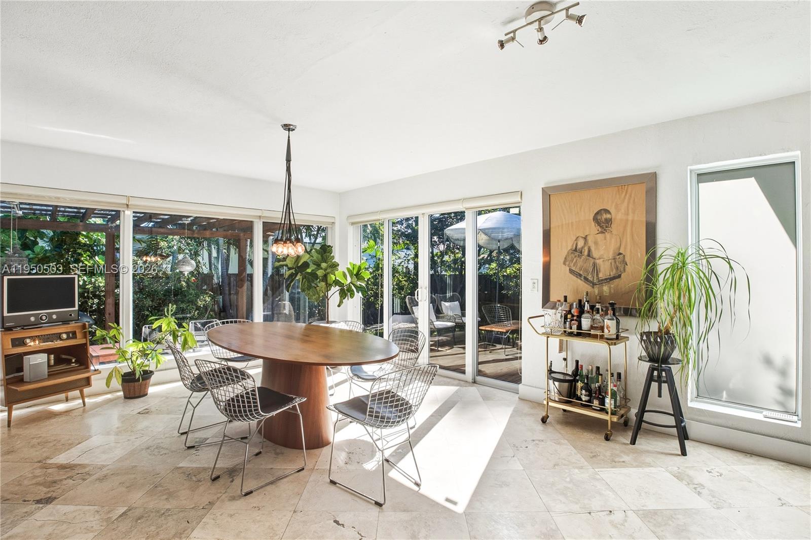 A dining room features a wooden oval table, wire chairs, and large glass sliding doors — 1106 NE 86th St, Miami FL 33138, MIAMI, FL