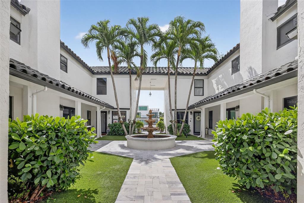 A courtyard features a central fountain, palm trees, and a stone walkway between white buildings — 1524 SE 12TH STREET UNIT 6, FORT LAUDERDALE, FL