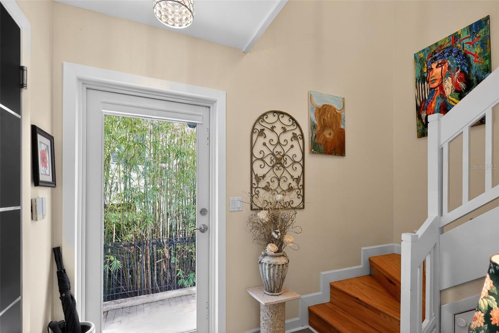 An entryway features a glass-paned door, wooden stairs, decorative wall art, and a pedestal vase — 1524 SE 12TH STREET UNIT 6, FORT LAUDERDALE, FL