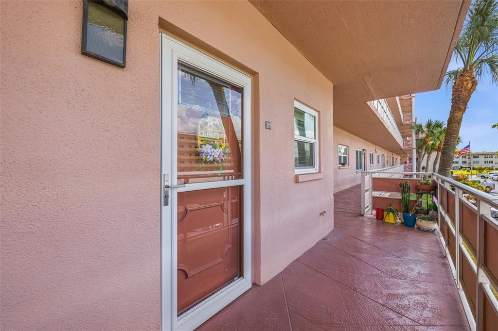 An exterior view of a pink apartment building balcony with a door labeled 212 — 5521 80TH STREET N UNIT 212, ST PETERSBURG, FL