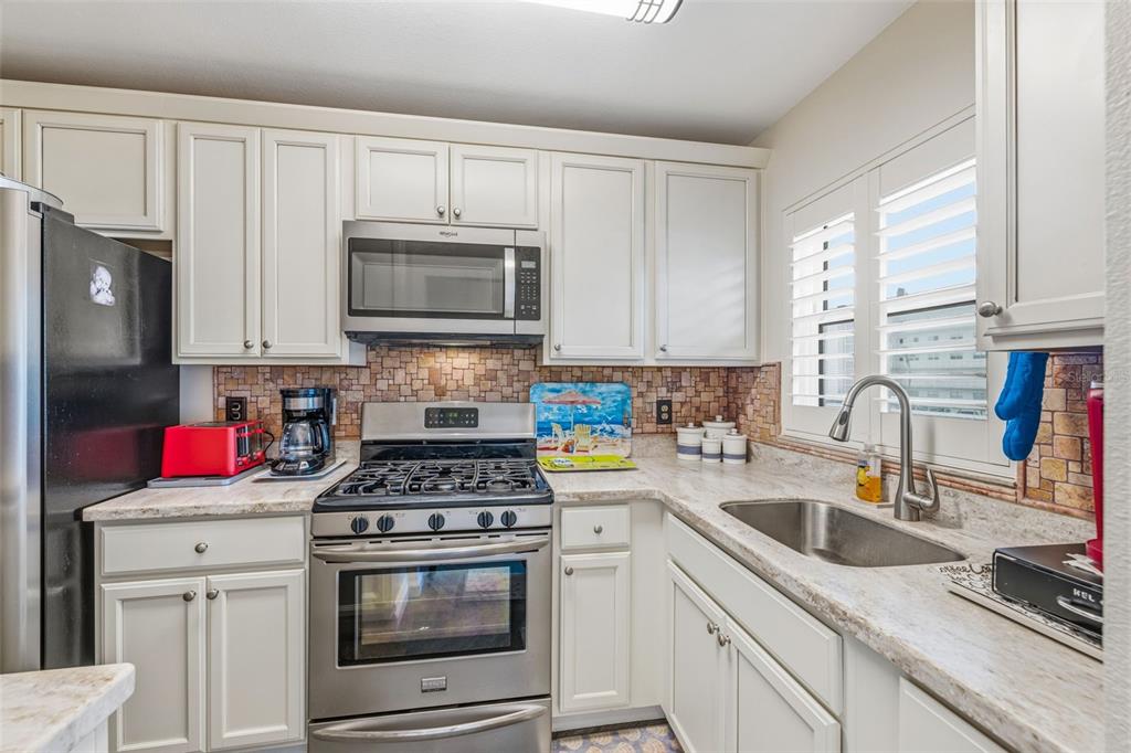 A kitchen features white cabinets, stainless steel appliances, a stone tile backsplash, and granite countertops — 5521 80TH STREET N UNIT 212, ST PETERSBURG, FL